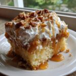 A delicious slice of butter pecan praline poke cake topped with whipped cream, caramel sauce, and chopped pecans.