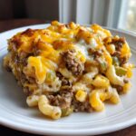 A close-up serving of baked cheeseburger casserole featuring elbow macaroni, ground beef, and a thick, bubbly layer of melted cheddar and white cheese.