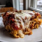 A close-up of a gooey, cheesy slice of pizza casserole with melted mozzarella dripping down the side.