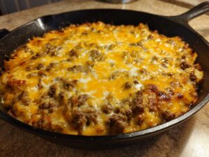 Close-up of baked Cheesy Taco Potatoes topped with melted cheddar and ground meat in a black cast iron skillet.