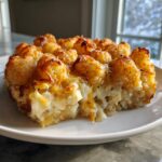 A close-up slice of cheesy tater tot casserole with crispy, golden brown tater tots on top.