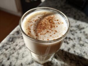 Close-up of a glass filled with creamy coquito, topped with a dusting of ground cinnamon.