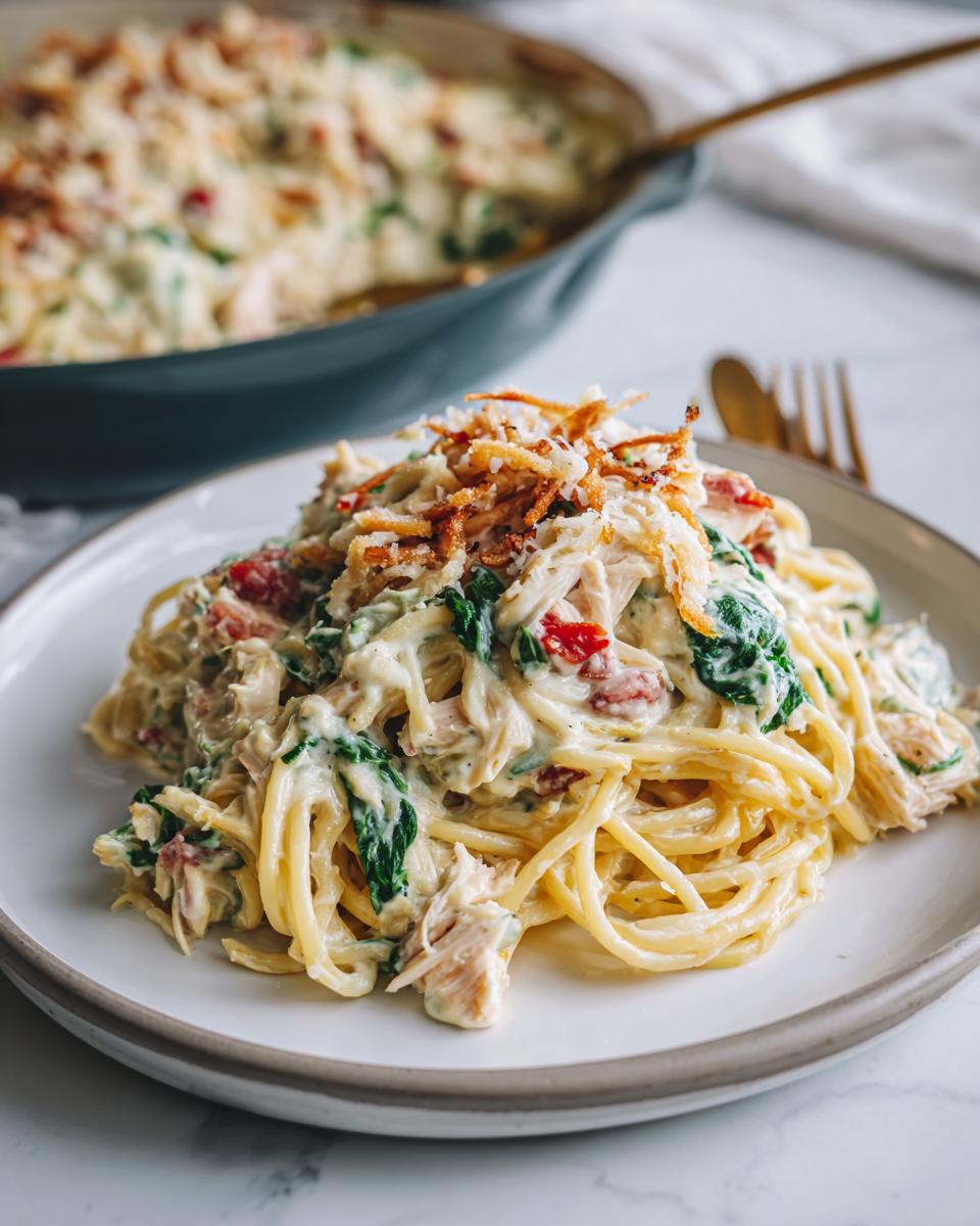A serving of creamy Monterey chicken spaghetti mixed with spinach and topped with crispy onions on a white plate.