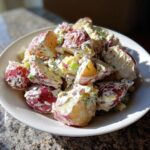 Close-up of creamy red potato salad chunks mixed with celery and red onion in a white bowl.