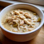 A close-up view of a white bowl filled with rich, creamy white chicken chili featuring shredded chicken and white beans.