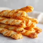 A close-up stack of golden brown, twisted, crispy cheese straws with visible baked cheese.