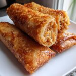 Close-up of four golden brown, crispy egg roll appetizers stacked on a white plate, showing the filling.