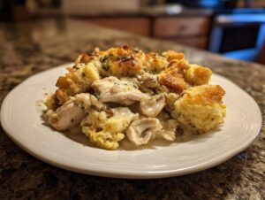 A close-up serving of creamy crock pot chicken and stuffing with golden stuffing pieces on a white plate.