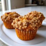 Three freshly baked sweet potato muffins topped with a thick layer of brown sugar streusel, resting on a white plate.