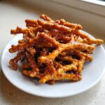 A pile of crunchy, glazed toffee pretzels sprinkled with sea salt, served on a small white plate.
