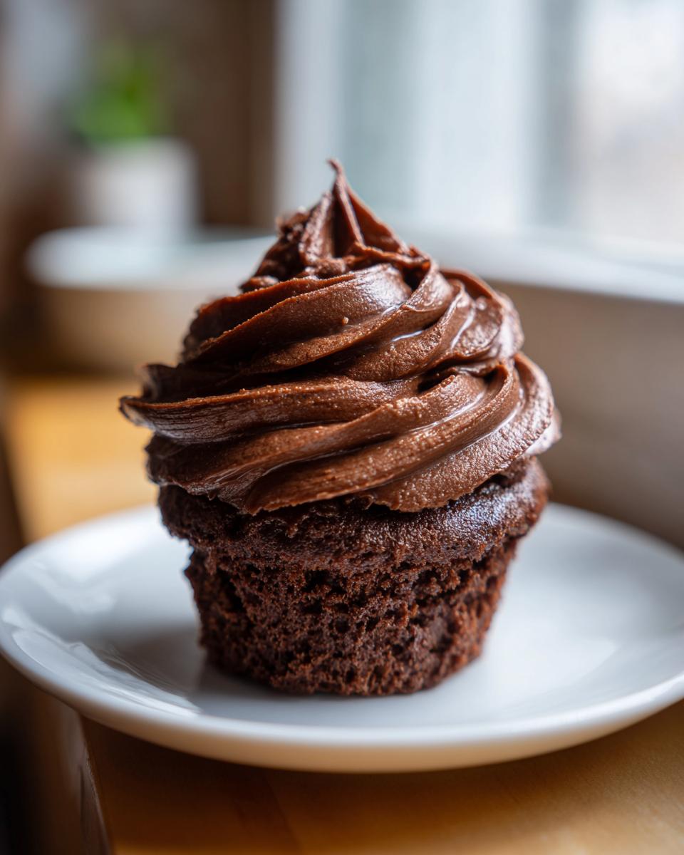 Close-up of a dark chocolate cupcake topped with a generous swirl of rich chocolate frosting.