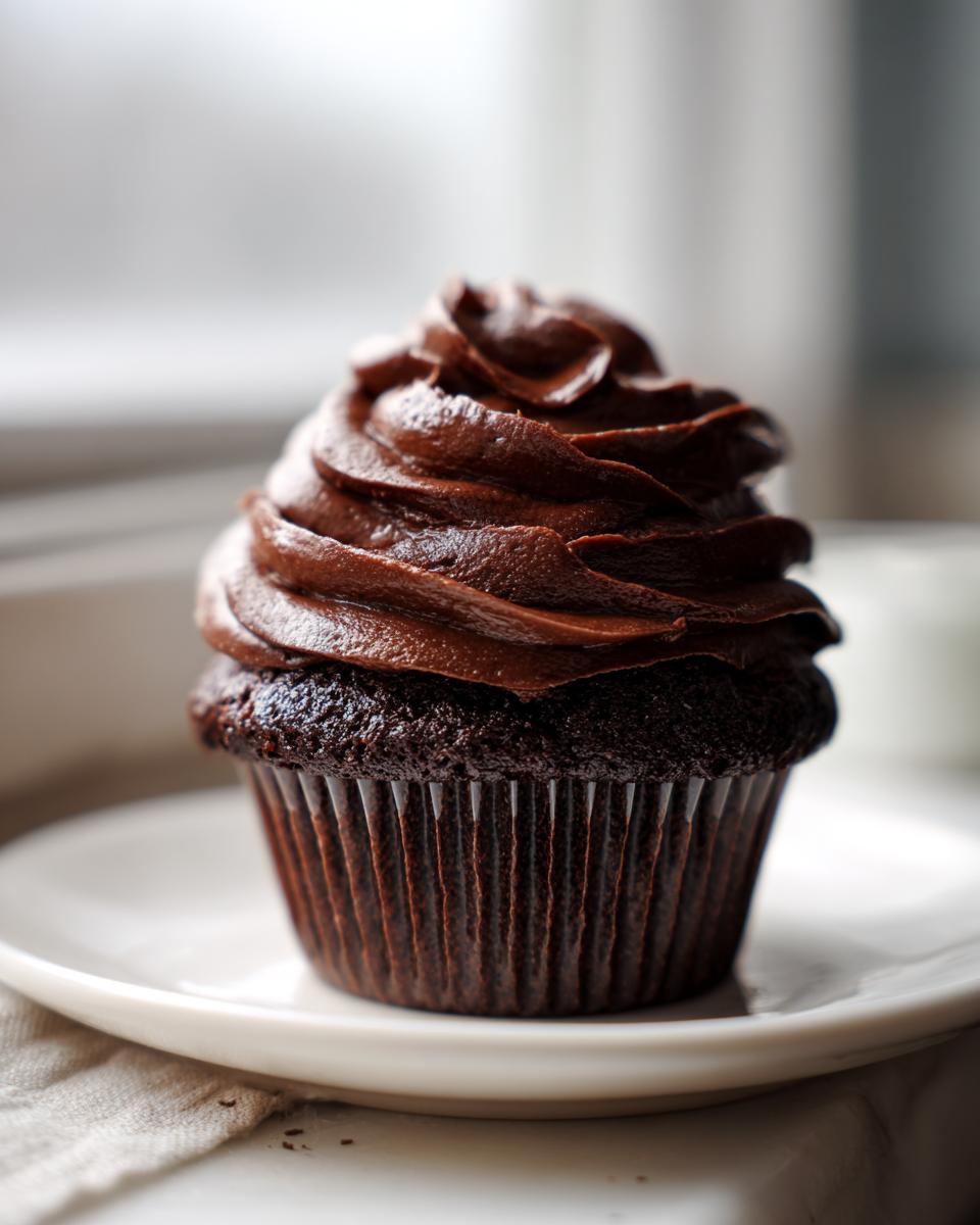 A dark chocolate cupcake topped with a generous swirl of rich, glossy chocolate frosting.