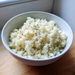 A white bowl filled with fluffy cauliflower rice, lightly seasoned with black pepper.
