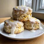 A stack of three fluffy lemon scones topped with thick white glaze and bright yellow lemon zest.
