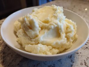 A close-up of incredibly fluffy mashed potatoes served in a white bowl on a granite countertop.