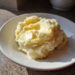 A generous serving of fluffy mashed potatoes topped with melting butter in a white bowl.