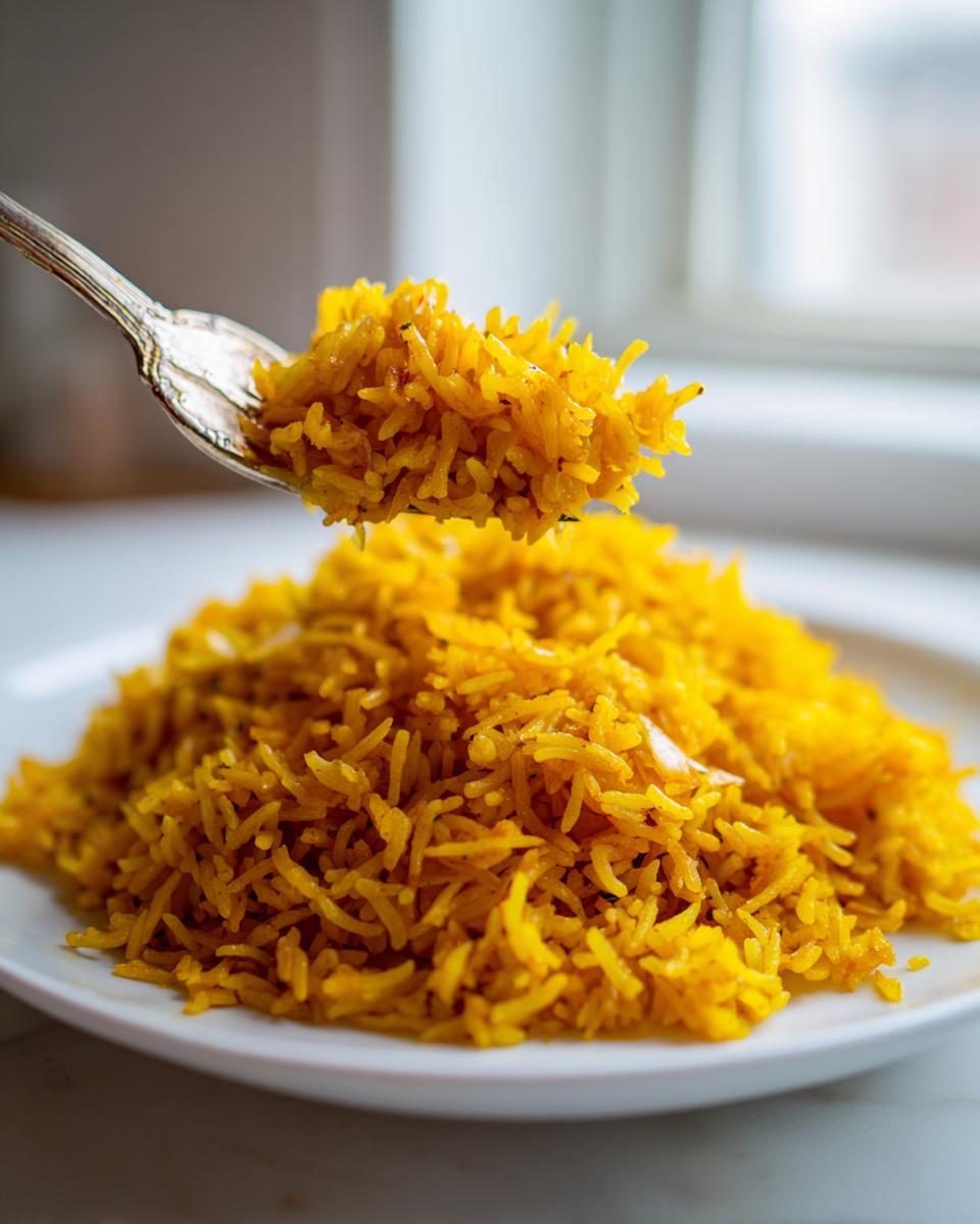 A fork lifting a bite of vibrant yellow turmeric rice over a plate piled high with more seasoned turmeric rice.