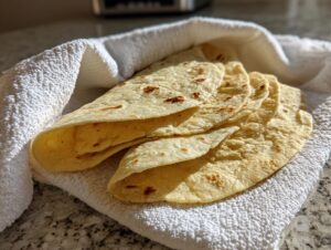 A stack of warm, freshly made corn tortillas wrapped in a white kitchen towel.
