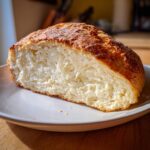 Close-up of a freshly baked loaf of soda bread, cut in half to show the soft, white interior and golden crust.