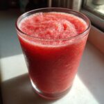 A tall glass filled with a bright red, icy frozen strawberry daiquiri, showing condensation on the outside.