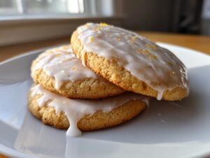 Three glazed earl grey cookies stacked on a white plate, topped with lemon zest.