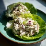 Two servings of creamy greek yogurt chicken salad scooped into crisp lettuce cups on a teal plate.
