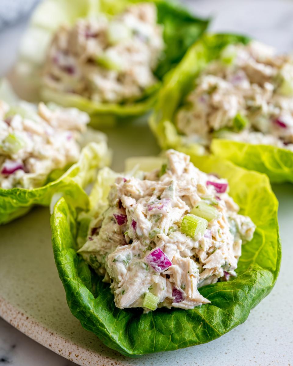 Close-up of creamy greek yogurt chicken salad served in crisp lettuce cups with visible celery and red onion.