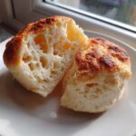 Close-up of a homemade english muffin split in half, showing its airy, open crumb structure.