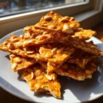 A stack of broken, golden pieces of homemade peanut brittle recipe, glistening in sunlight.