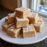 A tempting stack of homemade peanut butter fudge squares dusted lightly with powdered sugar, resting on a white plate.