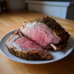 A juicy, medium-rare rib roast, crusted with herbs, sliced open to show the pink interior, resting on a white plate.