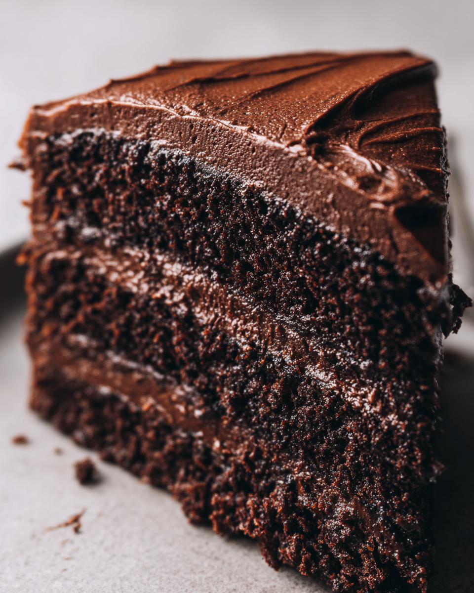 Close-up of a decadent slice of chocolate fudge cake showing moist layers and rich chocolate frosting.