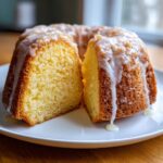 A slice cut from a moist lemon pound cake drizzled generously with white glaze, sitting on a white plate.