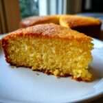 Close-up of a moist, golden slice of olive oil cake on a white plate, showing its crumb texture.