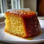 Close-up of a moist, golden slice from a rum cake recipe, generously drizzled with a shiny glaze.