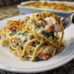 A fork lifting a creamy bite of Monterey chicken spaghetti, showing shredded chicken, spinach, and crispy topping.