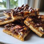 A stack of rich Pecan Pie Bark bars featuring a shortbread crust, caramel, pecans, and a chocolate drizzle.