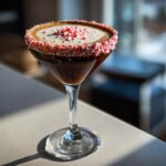 A rich peppermint espresso martini in a coupe glass, featuring a crushed candy cane rim and topping.