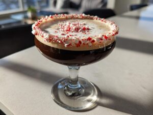 A rich peppermint espresso martini in a coupe glass, featuring a thick foam top and a rim coated in crushed candy canes.
