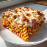 A square serving of baked pizza pasta casserole topped with melted mozzarella and pepperoni slices.