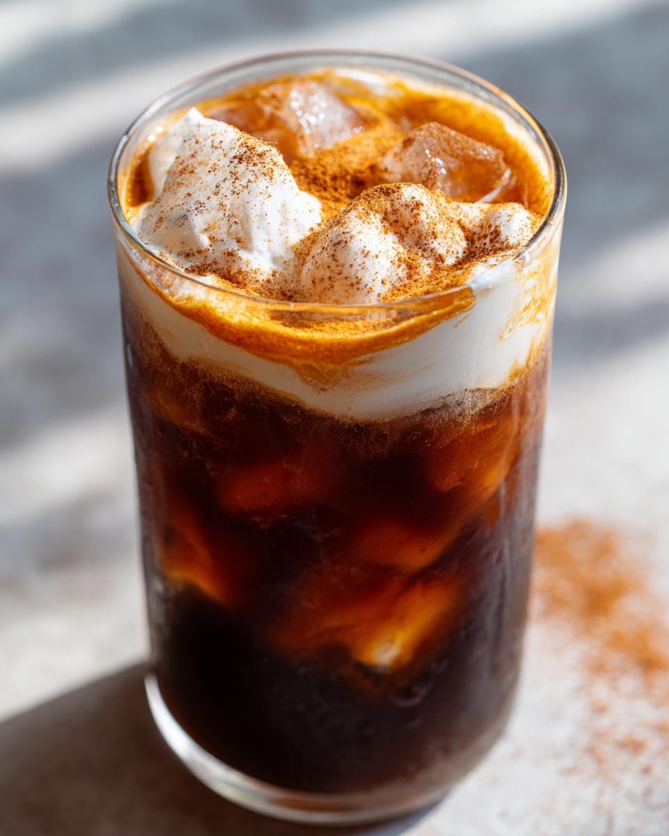 Close-up of a tall glass filled with iced pumpkin cream cold brew, topped with whipped cream and cinnamon.