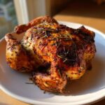 A beautifully roasted spatchcock chicken with crispy, golden-brown skin seasoned with herbs, resting on a white plate.