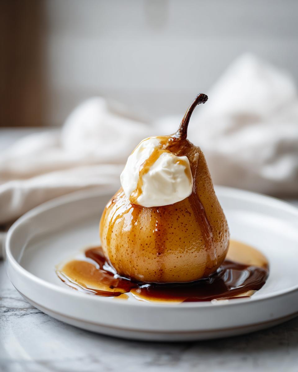 A single, beautifully caramelized poached pear topped with a dollop of cream and drizzled with rich syrup, served on a white plate.