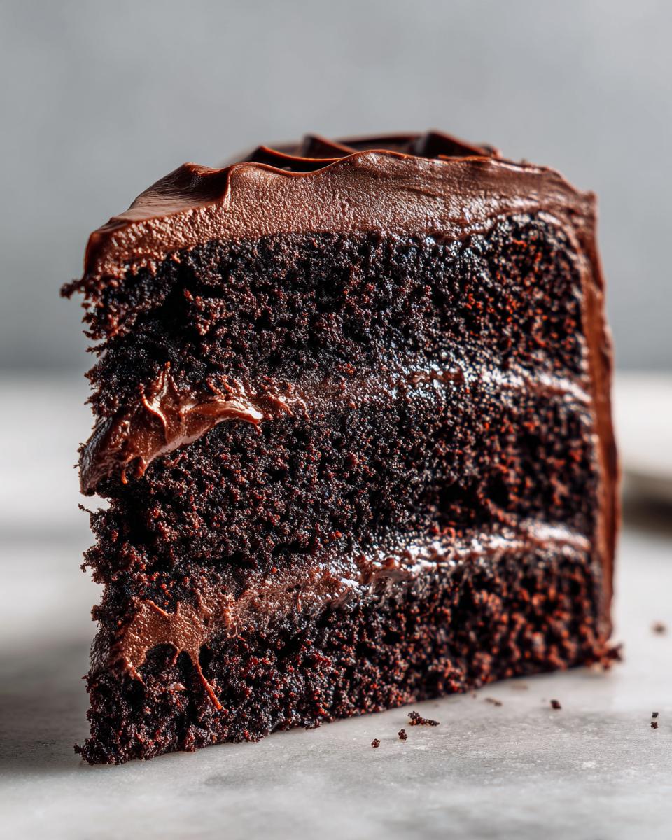 Close-up of a moist slice of three-layer chocolate fudge cake covered in thick, glossy chocolate frosting.