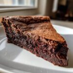A decadent slice of hot fudge pie showing a rich, molten chocolate center and a slightly cracked top.