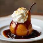 A beautifully presented single poached pear topped with whipped cream, caramel sauce, and a sprinkle of zest.