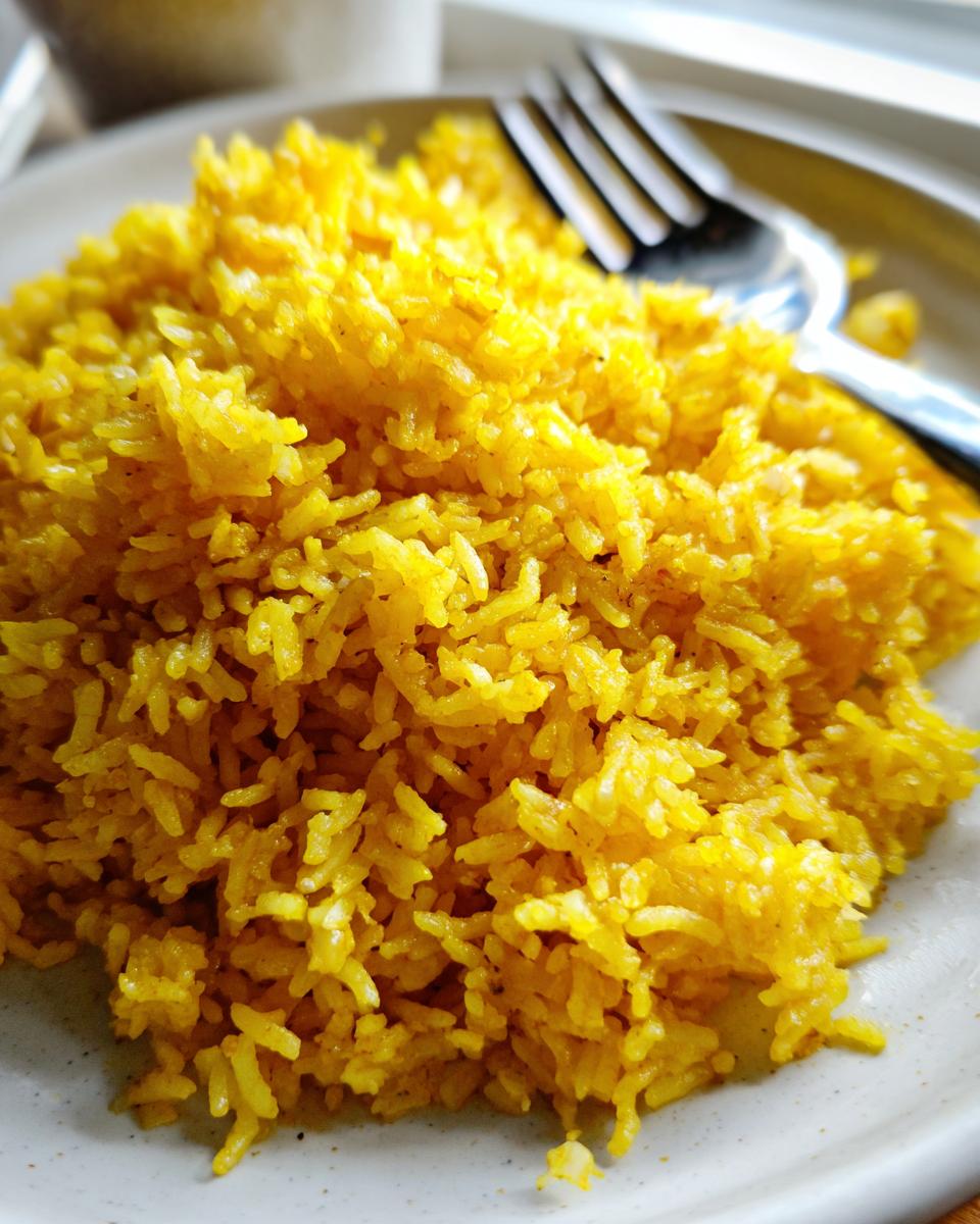 Close-up of fluffy, bright yellow turmeric rice served on a light-colored plate with a fork visible in the background.