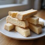 A close-up stack of golden brown, rectangular 3 ingredient shortbread cookies on a white plate.
