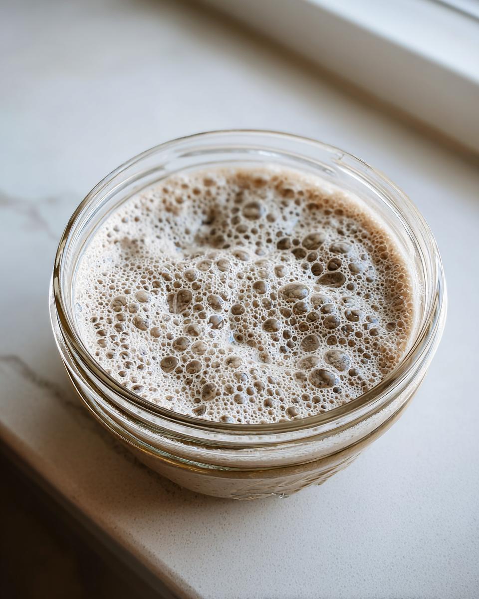 Close-up overhead view of an active sourdough starter in a glass jar, showing a thick layer of bubbles.