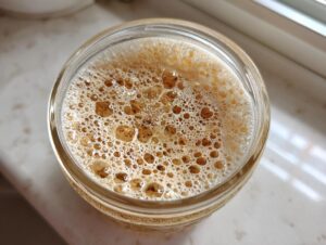 Overhead view of an active sourdough starter showing many brown and white bubbles in a glass jar.